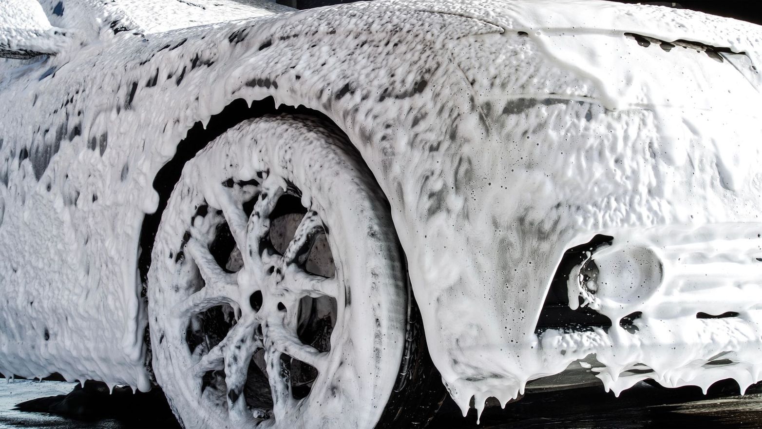 Hand washing a black car door with blue sponge mitt, soap suds and water dripping down