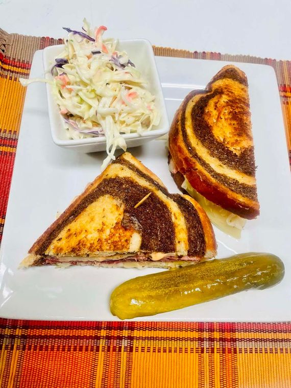 A grilled cheese sandwich with coleslaw and a pickle on a plate.