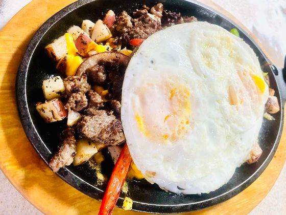 A plate of food with eggs , meat and potatoes on a wooden table.