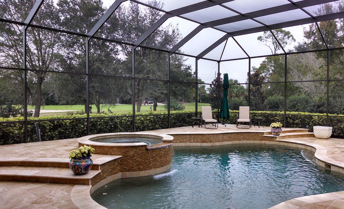 A large swimming pool with a screened in area and a hot tub.