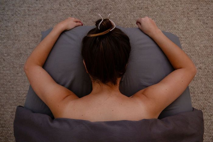 Person lying face down on a gray pillow with arms outstretched under a dark blanket.
