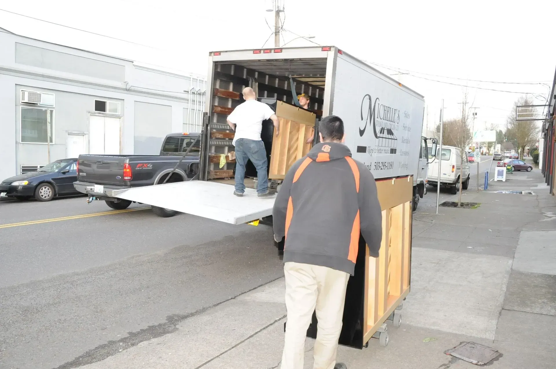 A man is pushing a piano out of a movers truck