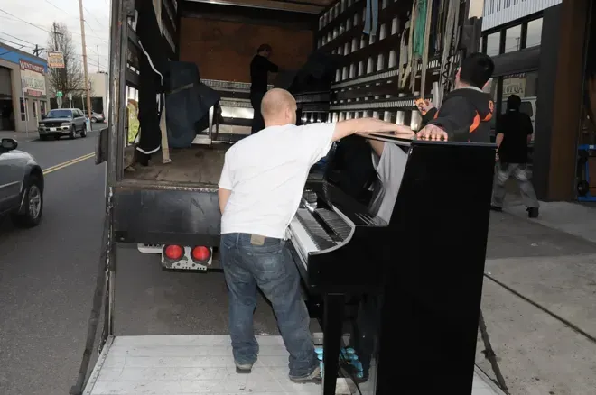 A man is pushing a piano out of the back of a truck.