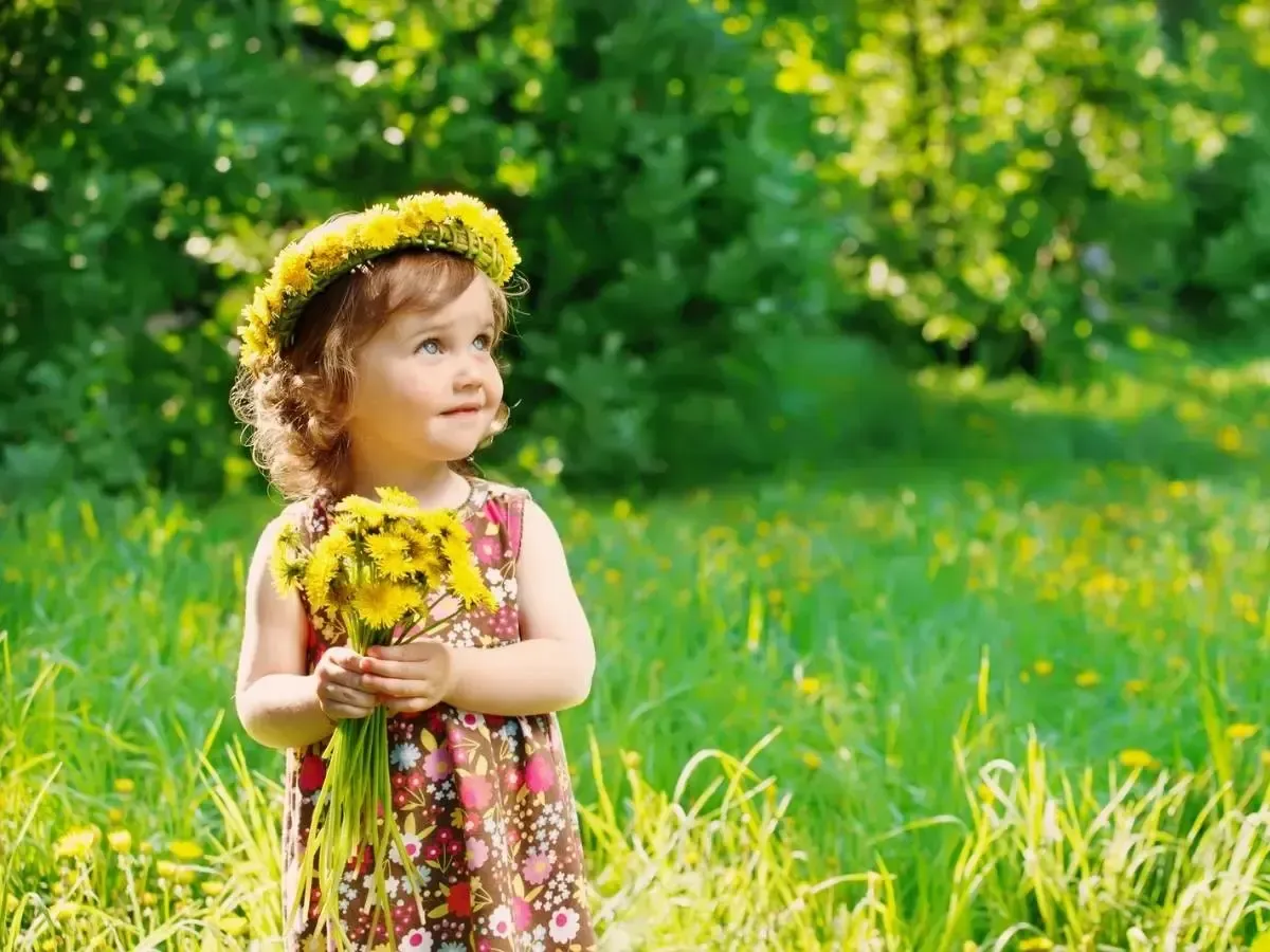 An immunocompromised little girl stands in a field holding flowers, in a toxin-free environment.