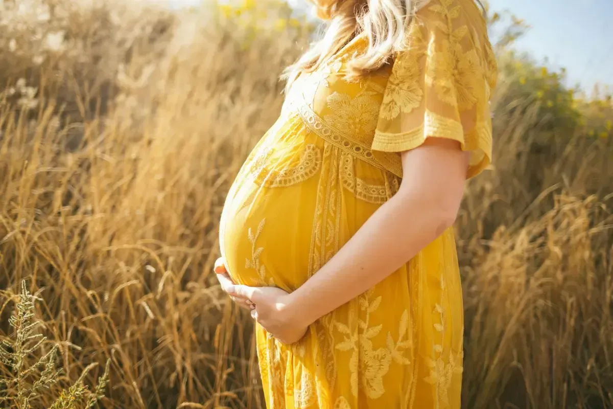 A pregnant woman holding her belly in a yellow dress