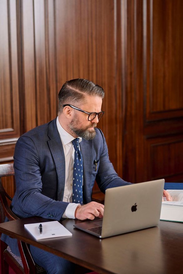Sævar Þór, lögmaður í jakkafötum og með bindi situr við skrifborð með fartölvu.