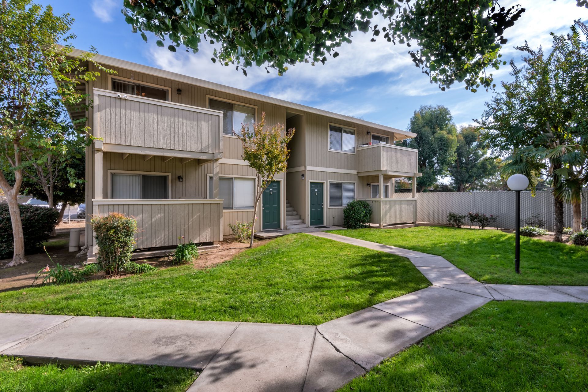 Two-story beige apartment building with balconies, green lawn, and paved walkway.