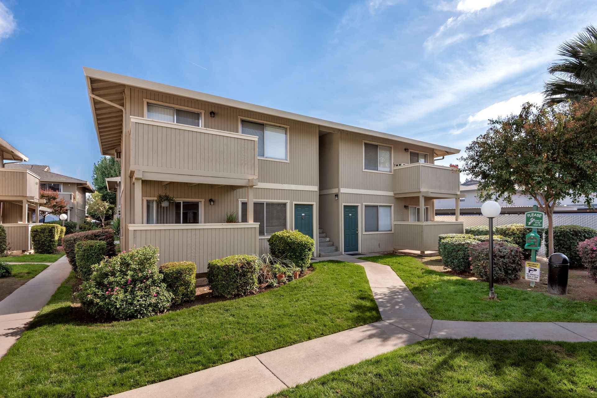 Two-story apartment building with balconies and green lawn under a blue sky.
