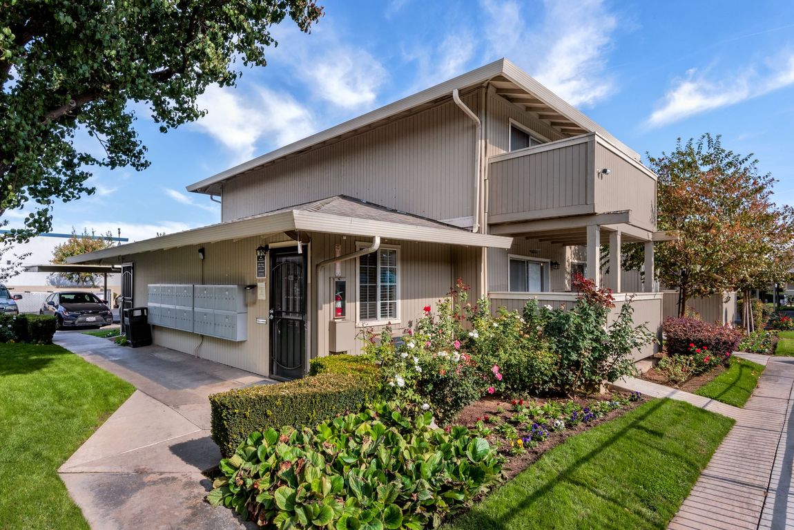 Two-story beige apartment building with landscaping and a sunny, blue sky.