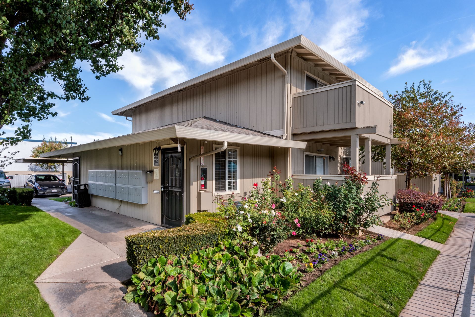 Two-story beige apartment building with landscaping and a sunny, blue sky.