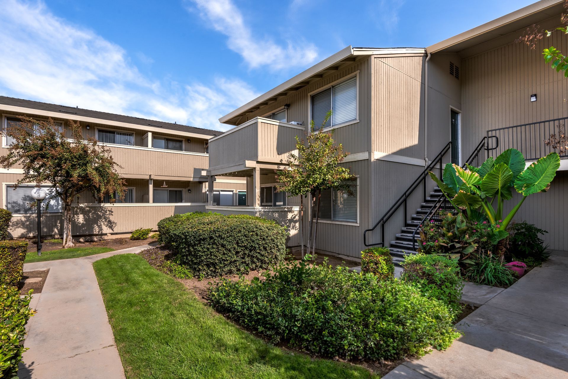 Apartment building exterior with beige walls, green landscaping, and a blue sky.