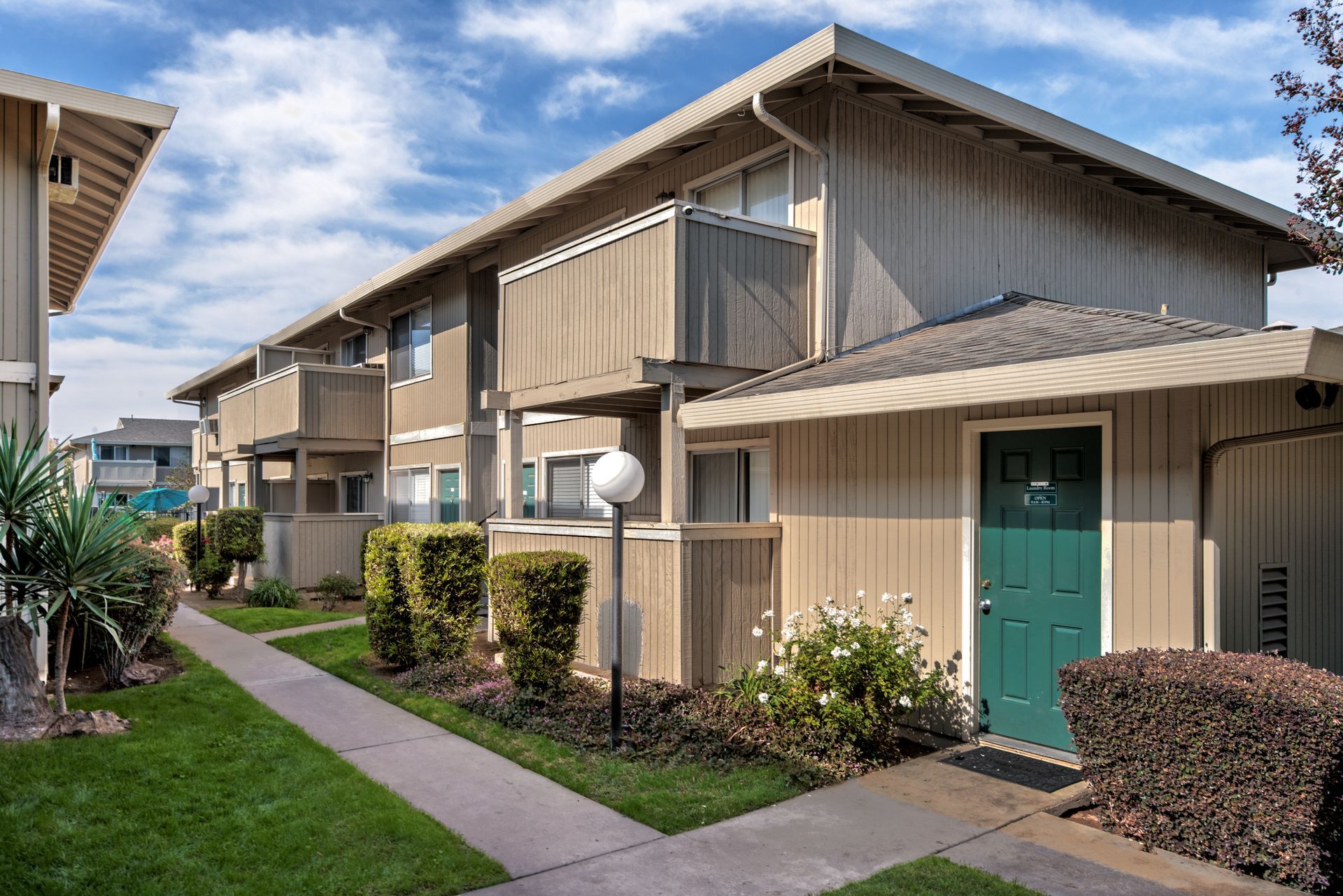 Apartment building with light-colored siding, balconies, and green front door under a blue sky.