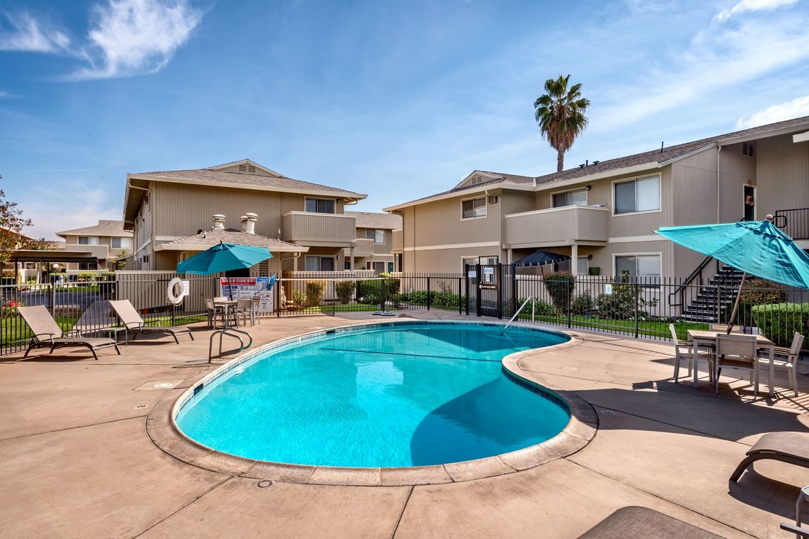 Apartment complex pool with blue water, lounge chairs, and umbrellas on a sunny day.