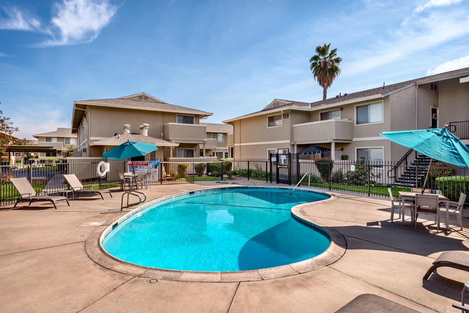 Apartment complex pool with blue water, lounge chairs, and umbrellas on a sunny day.