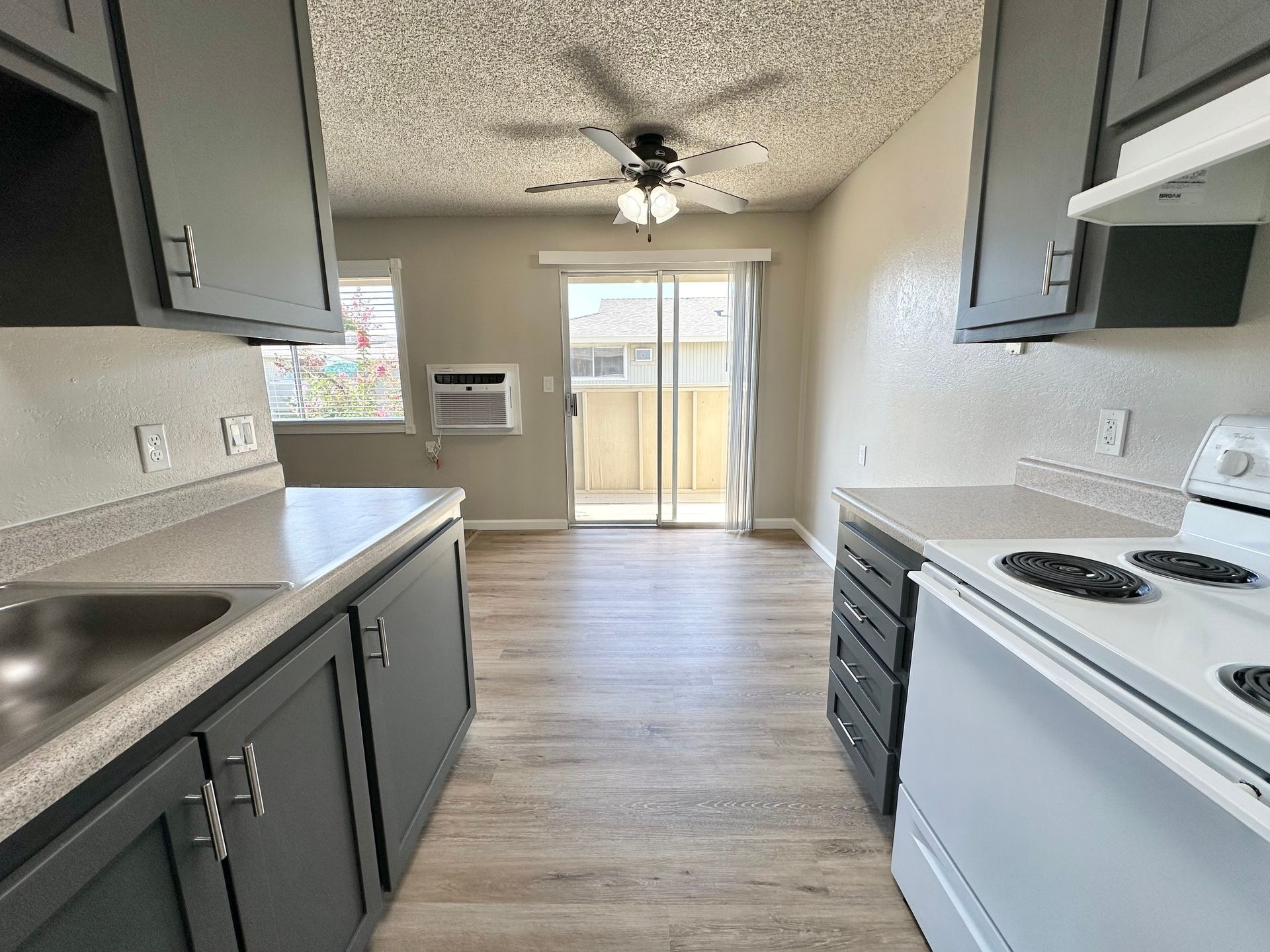 Kitchen interior with gray cabinets, white appliances, and a sliding door to a balcony.