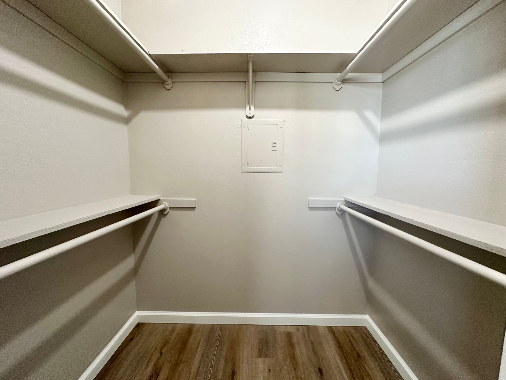 Empty walk-in closet with white shelves, rods, and walls. Light wood-look floor.