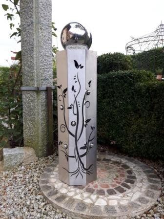 Eine Edelstahlsäule mit einer Kugel darauf in einem Garten.