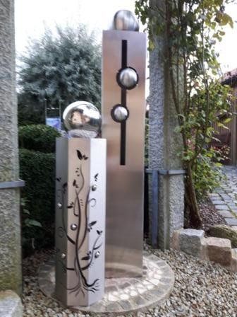 Eine Edelstahlskulptur mit einem Baum und Vögeln darauf