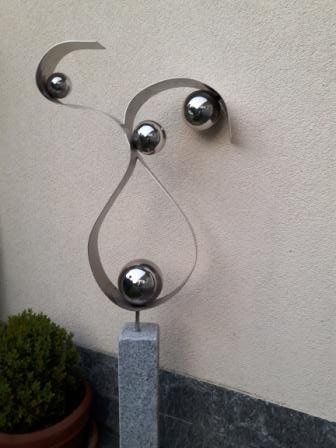 Eine Skulptur aus Edelstahl steht auf einem Granitsockel vor einer Wand.