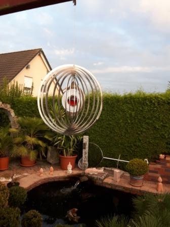 Eine große Skulptur aus Edelstahl steht neben einem Teich in einem Garten.