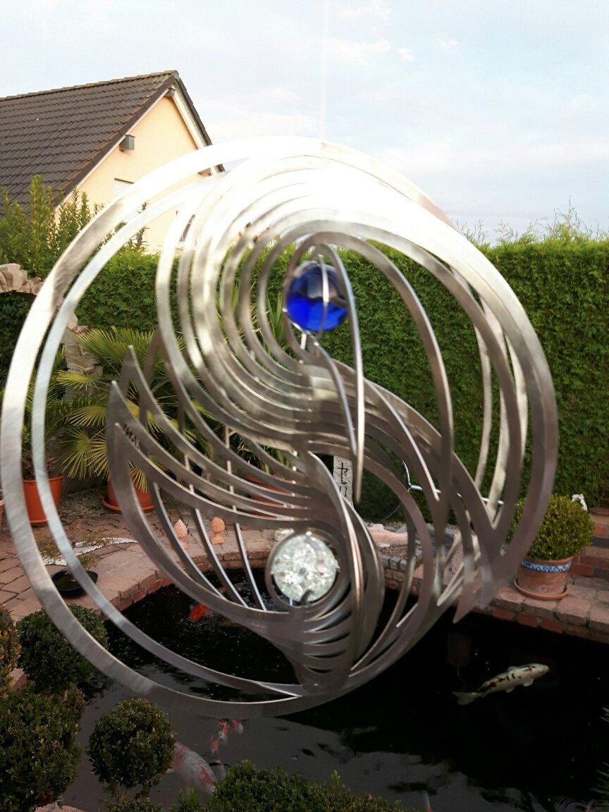 Vor einem Teich steht eine große Skulptur aus Edelstahl.