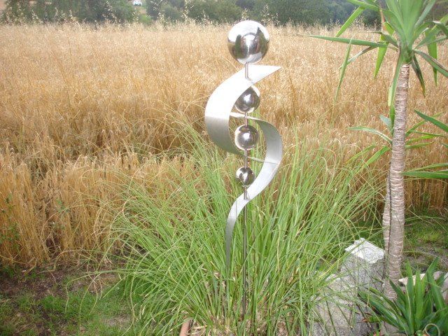 Eine Skulptur aus Edelstahl sitzt im Gras vor einem Feld.