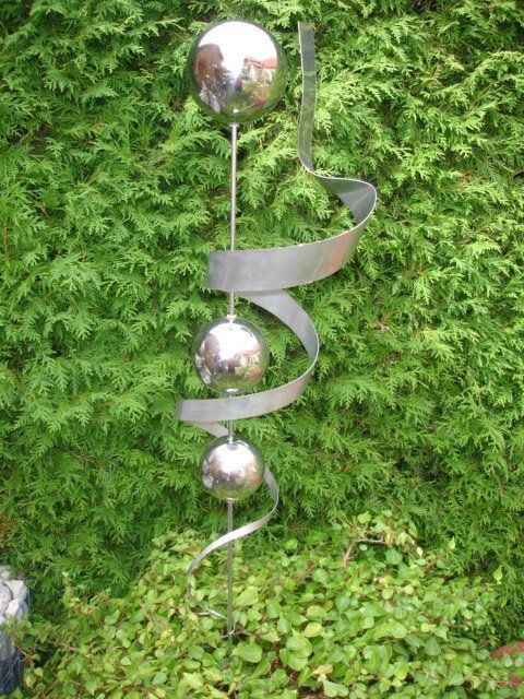 Eine Edelstahlskulptur sitzt vor einem grünen Busch.