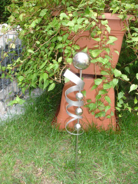 Eine Metallskulptur sitzt im Gras neben einer Topfpflanze