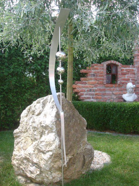 Auf einem großen Felsen sitzt eine Skulptur aus Edelstahl.