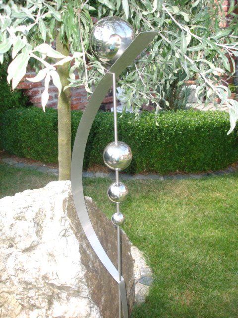 Eine Edelstahlskulptur sitzt auf einem Felsen in einem Garten