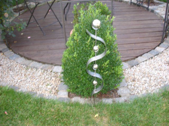 Eine Metallskulptur steht neben einem Busch in einem Garten.