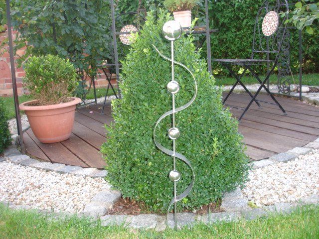 Eine Edelstahlskulptur in einem Garten neben einem Busch