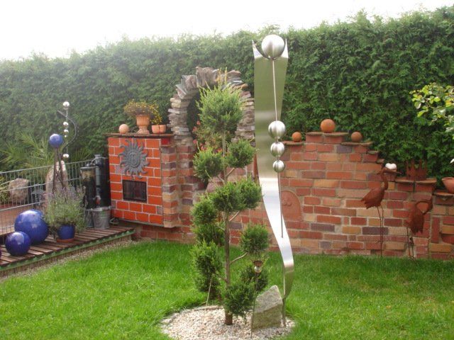 Eine Skulptur aus Edelstahl steht inmitten eines üppig grünen Gartens.