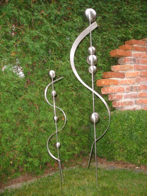 Eine Skulptur aus Edelstahl sitzt im Gras vor einer Backsteinmauer.