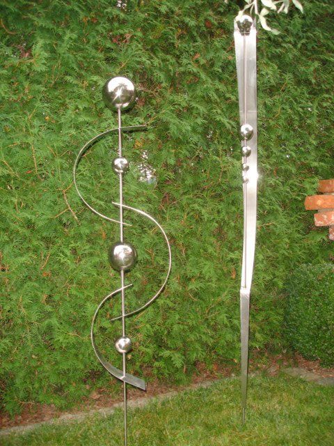 Zwei Skulpturen aus Edelstahl stehen auf einem üppigen grünen Rasen.