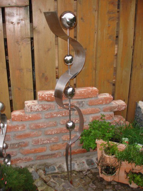 Eine Edelstahlskulptur steht vor einer Backsteinmauer