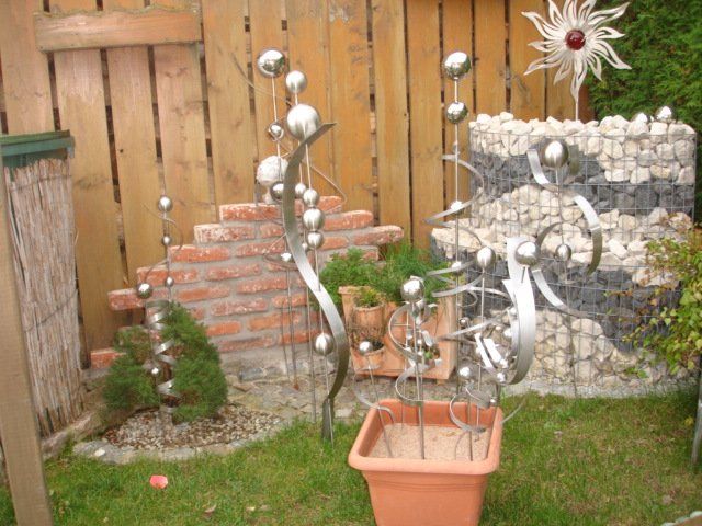 Eine Topfpflanze steht im Gras vor einem Zaun.