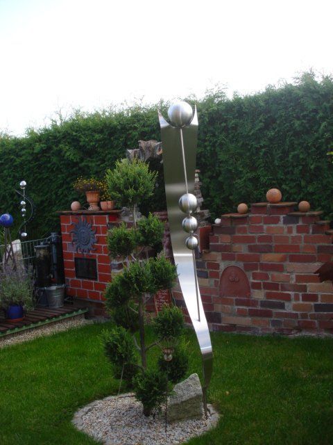 Eine Edelstahlskulptur in einem Garten mit einer Backsteinmauer im Hintergrund