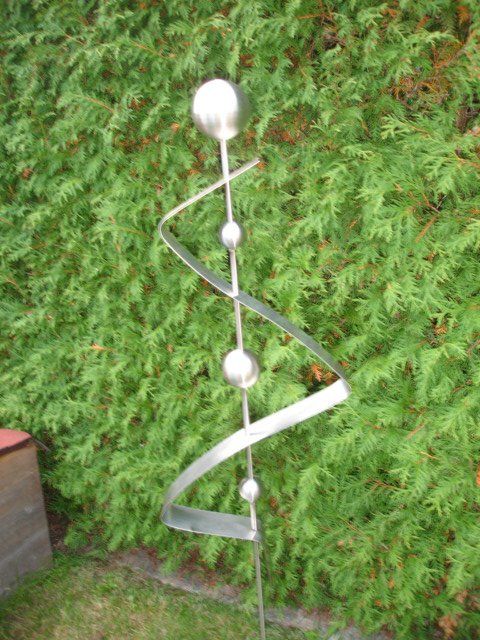 Eine Edelstahlskulptur sitzt vor einem grünen Busch.