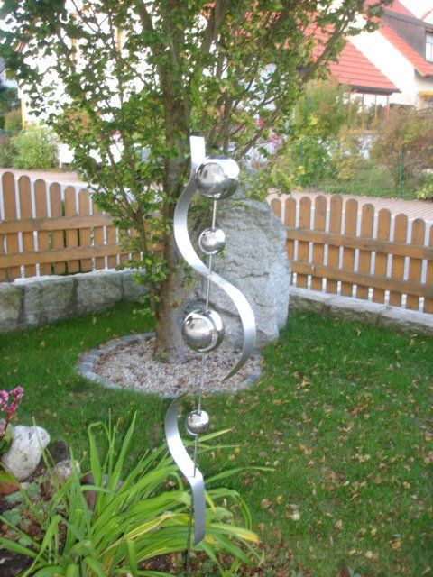 Eine Metallskulptur in einem Garten mit einem Holzzaun im Hintergrund