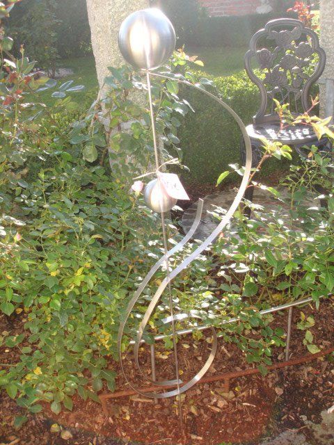 Eine Skulptur aus Edelstahl steht in einem Garten neben einer Bank.