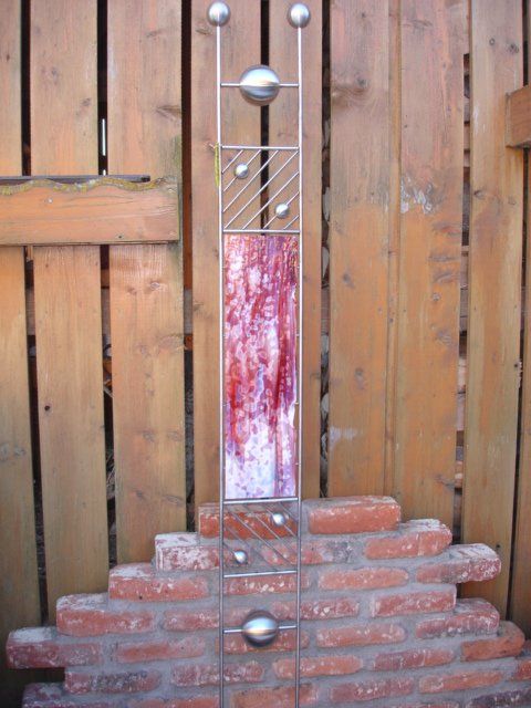 Eine Skulptur sitzt auf einer Ziegelmauer vor einem Holzzaun