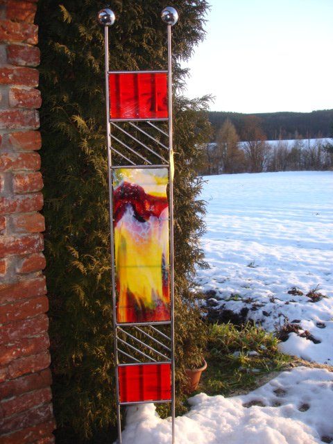 Eine Skulptur aus Buntglas sitzt im Schnee neben einer Backsteinmauer