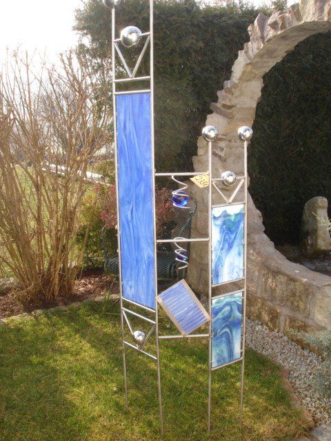 Eine Skulptur aus Edelstahl sitzt im Gras vor einem steinernen Torbogen.