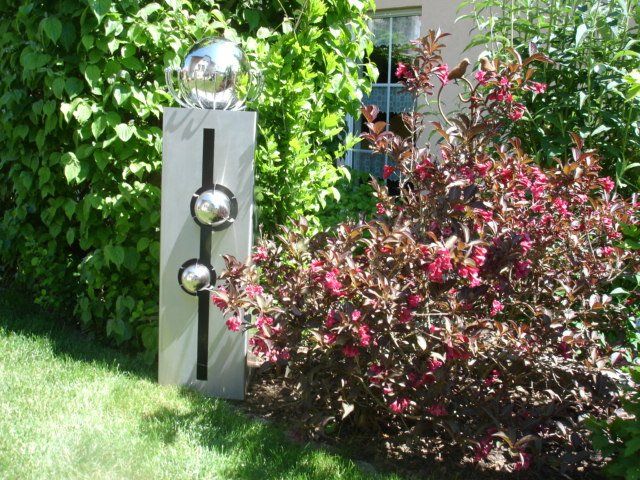 Eine Skulptur in einem Garten neben einem Busch mit rosa Blüten