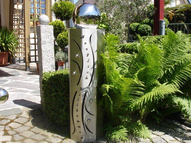 Eine Edelstahlskulptur ist von Farnen und Büschen umgeben