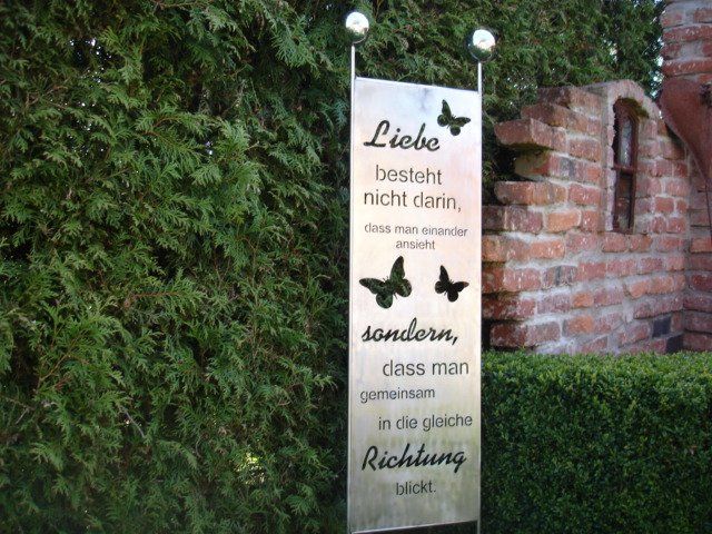 A sign that says liebe besteht nicht dann stands in front of a brick wall