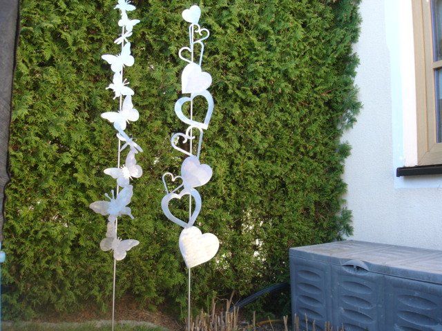Ein Haufen Herzen und Schmetterlinge auf Stöcken vor einem Busch.