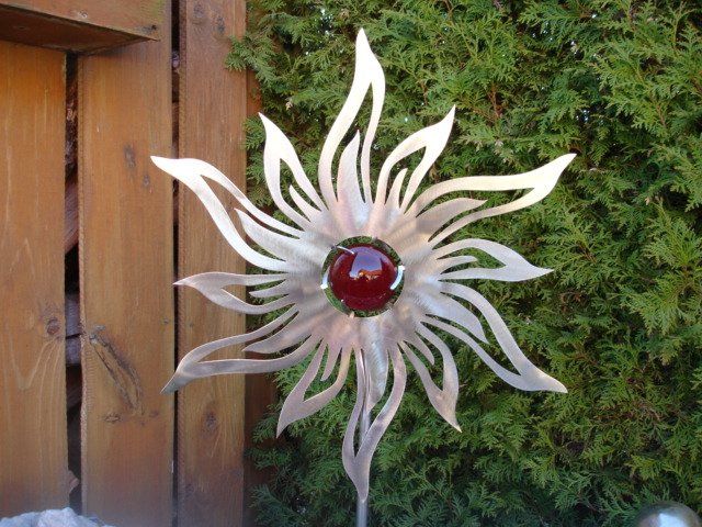 Eine Metallblume mit roter Mitte sitzt vor einem Holzzaun