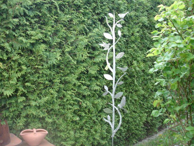 Eine Skulptur einer Pflanze mit Blättern steht vor einer Hecke